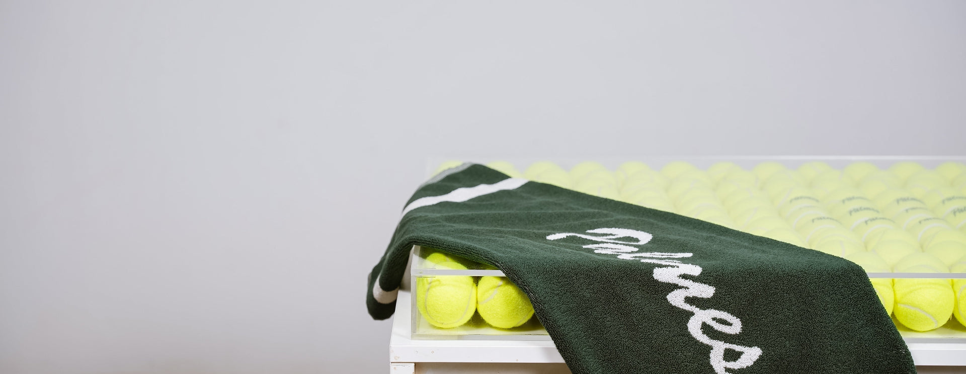 Green towel with 'Fitness' text on a white bench with yellow balls against a light gray background